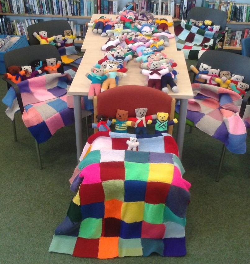 A display of handmade knittedquilts and small Teddy bears.